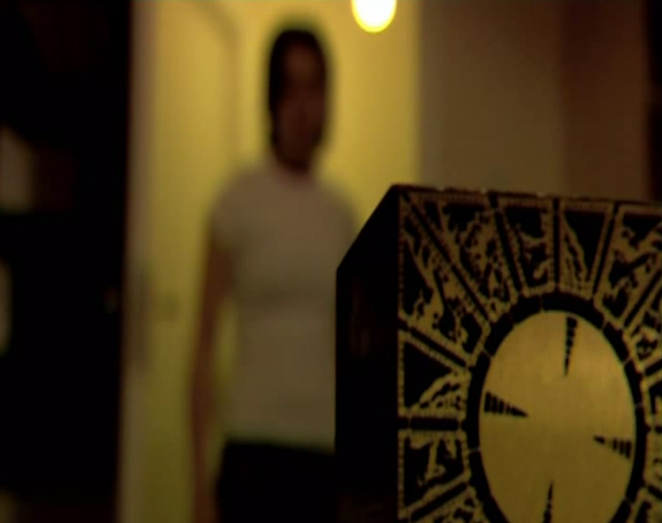 A still from The Hellraiser Chronicles: Lifebringer. A blurred figure enters a room, the strange device rests on the table inside.